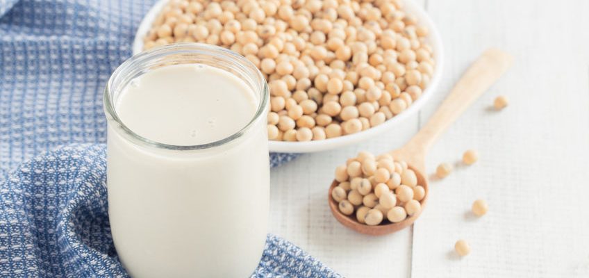 A glass of soy milk on a white wood floor with soybean as a background.